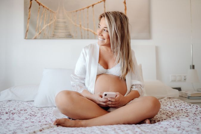 Smiling pregnant woman using smartphone at home