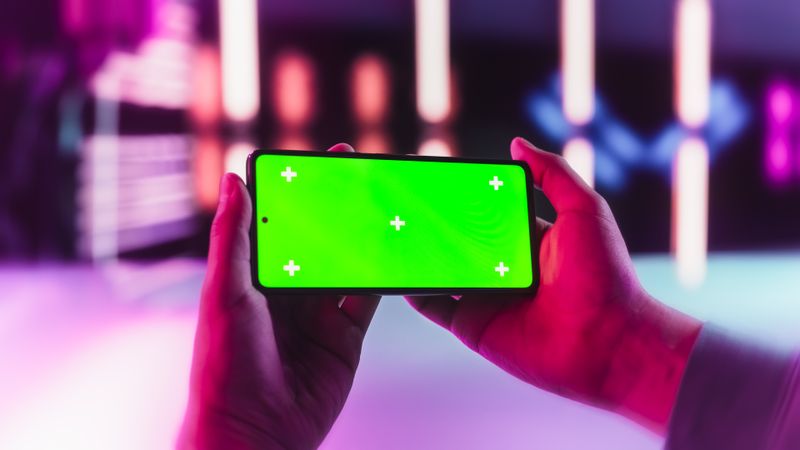 Stylish Person Holding a Modern Phone in Front of a Camera in a Neon Studio. Smartphone with Green Screen Chroma Key Display for Use in E-Learning and Educational Tutorials, Marketing and Advertising